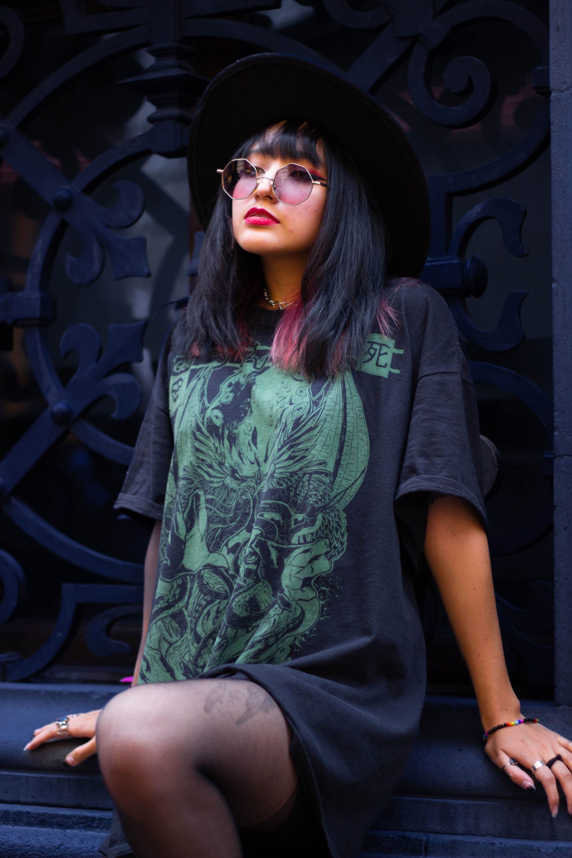 Fashionable young woman in goth style with sunglasses and hat, front view.
